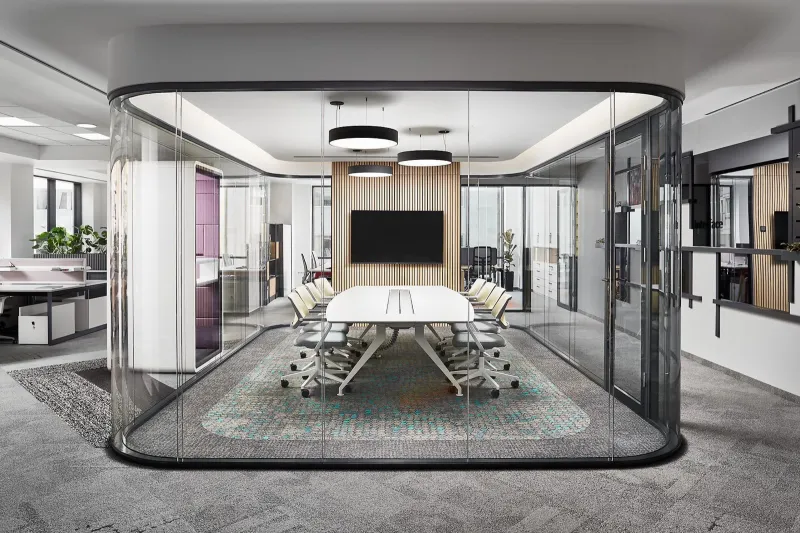 A glass-walled meeting room with a long table and a screen
