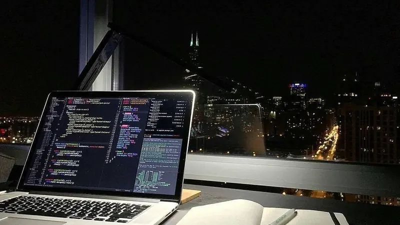 A laptop with code open by a window at night