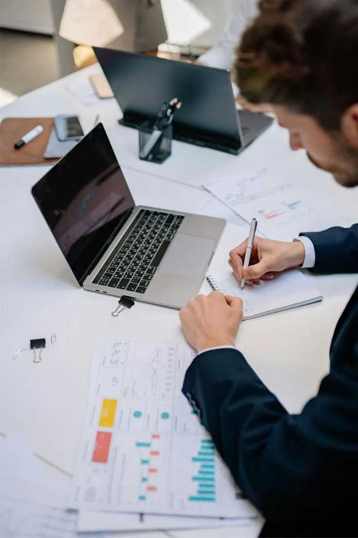 A professional reviewing business documents beside a laptop