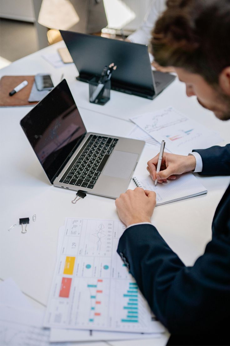 A person reviewing printed documents with a pen beside a laptop