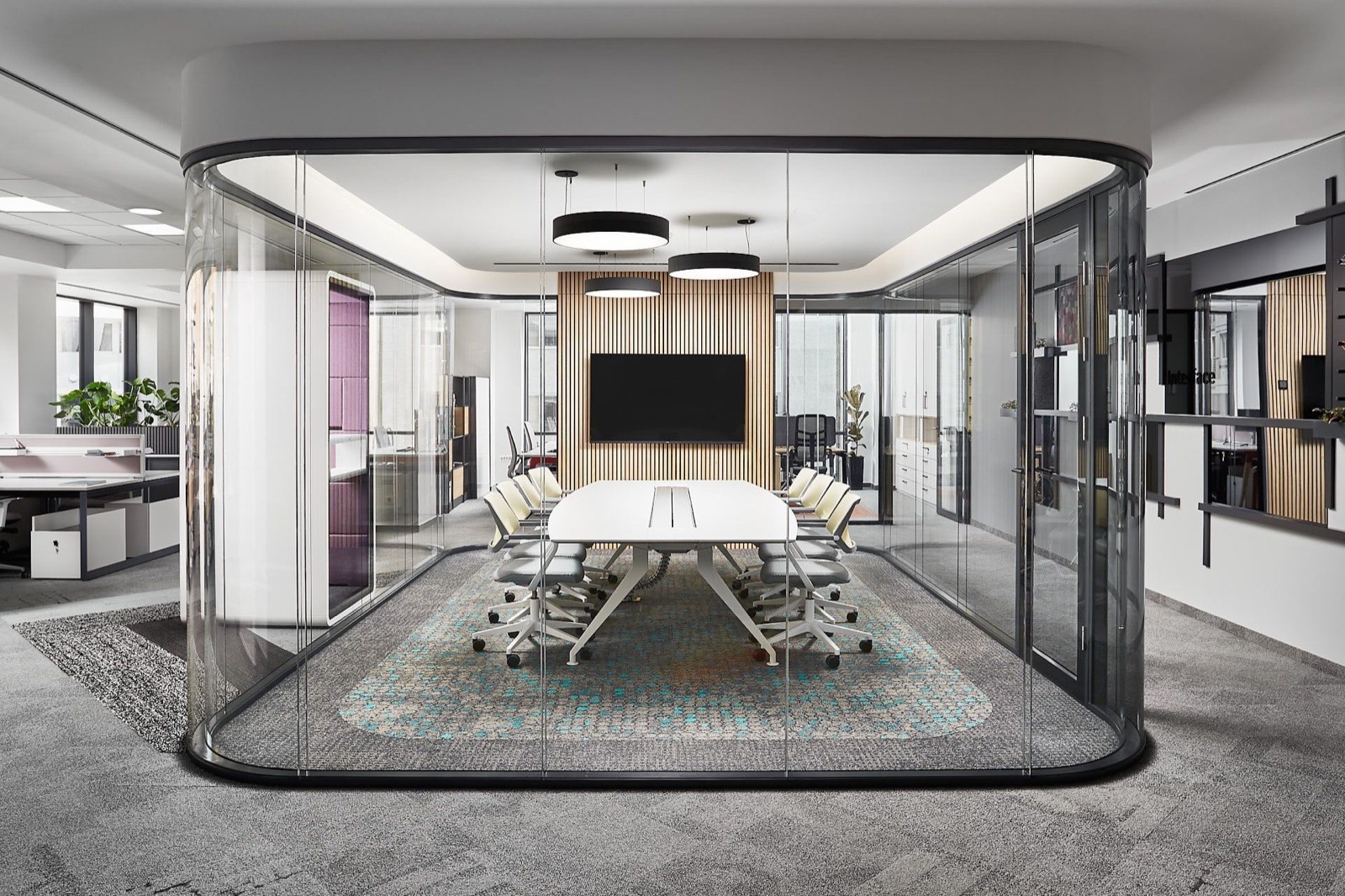 A glass-walled meeting room with a long table and a wall screen
