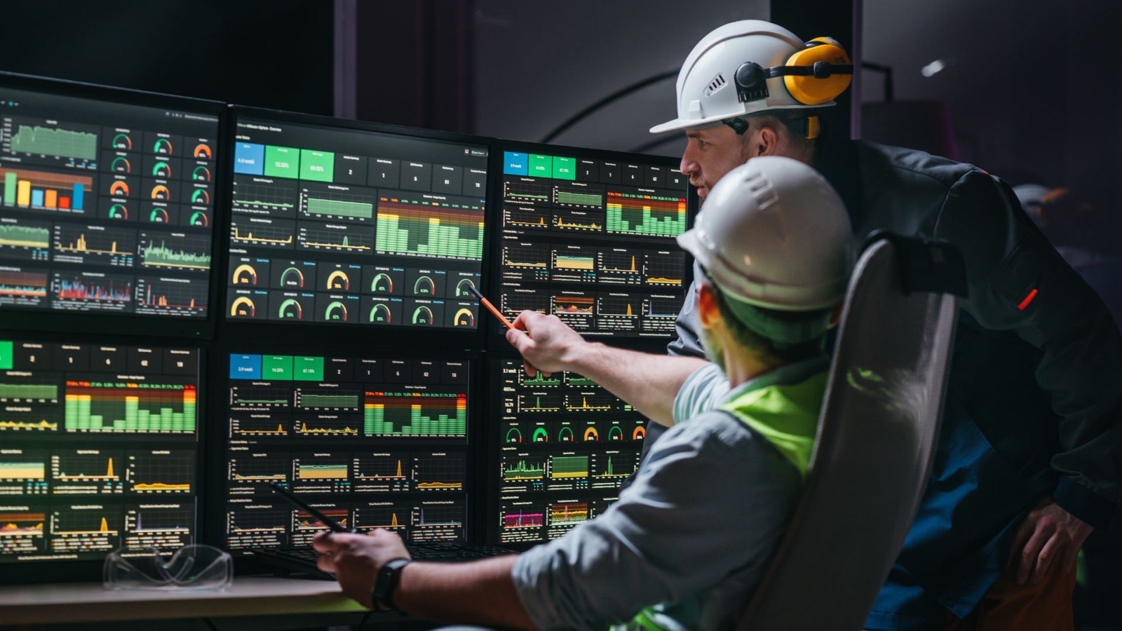 Operations staff in hard hats reviewing live dashboards in a control room