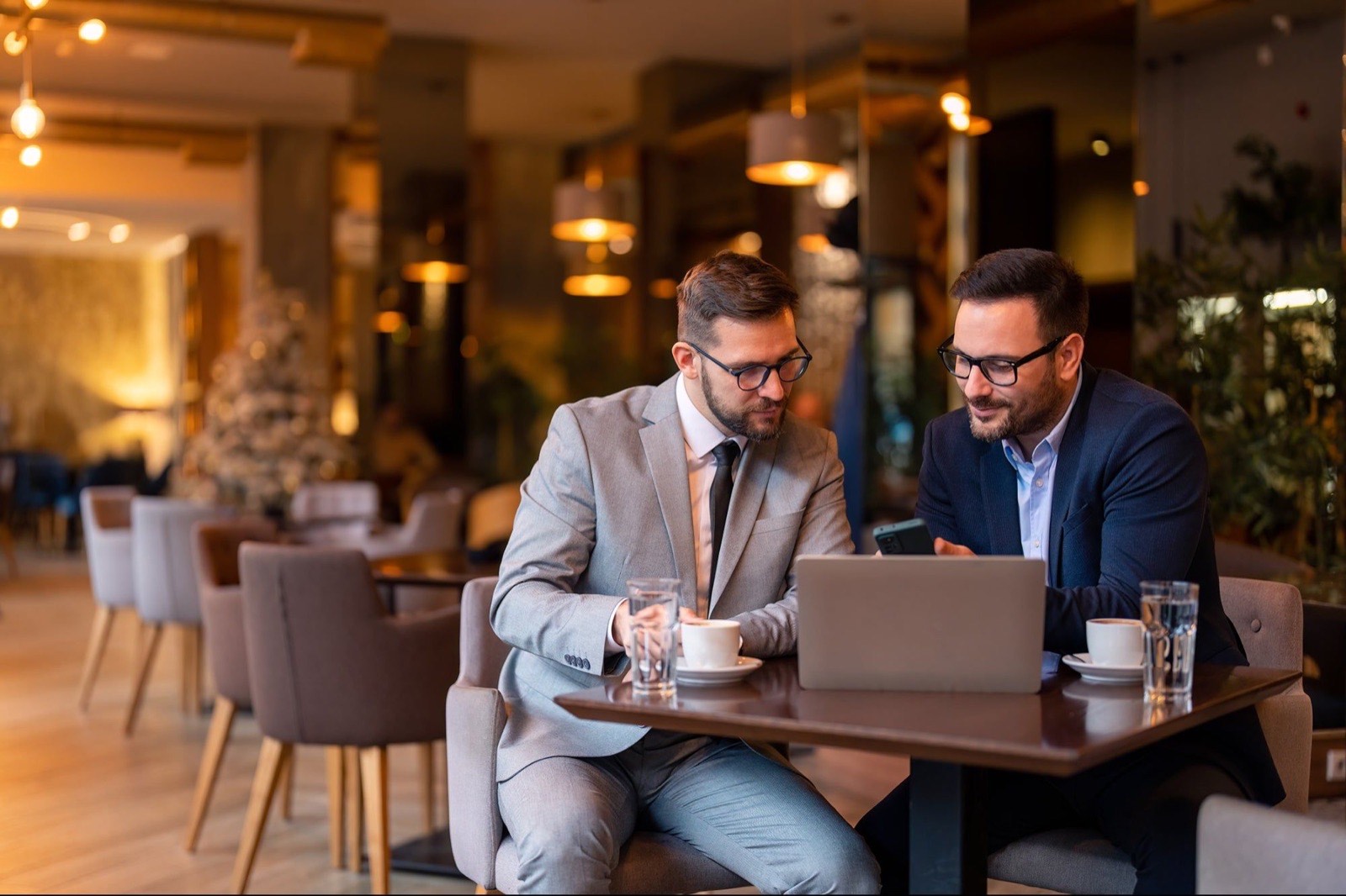 Two people reviewing a request together on a laptop in a cafe