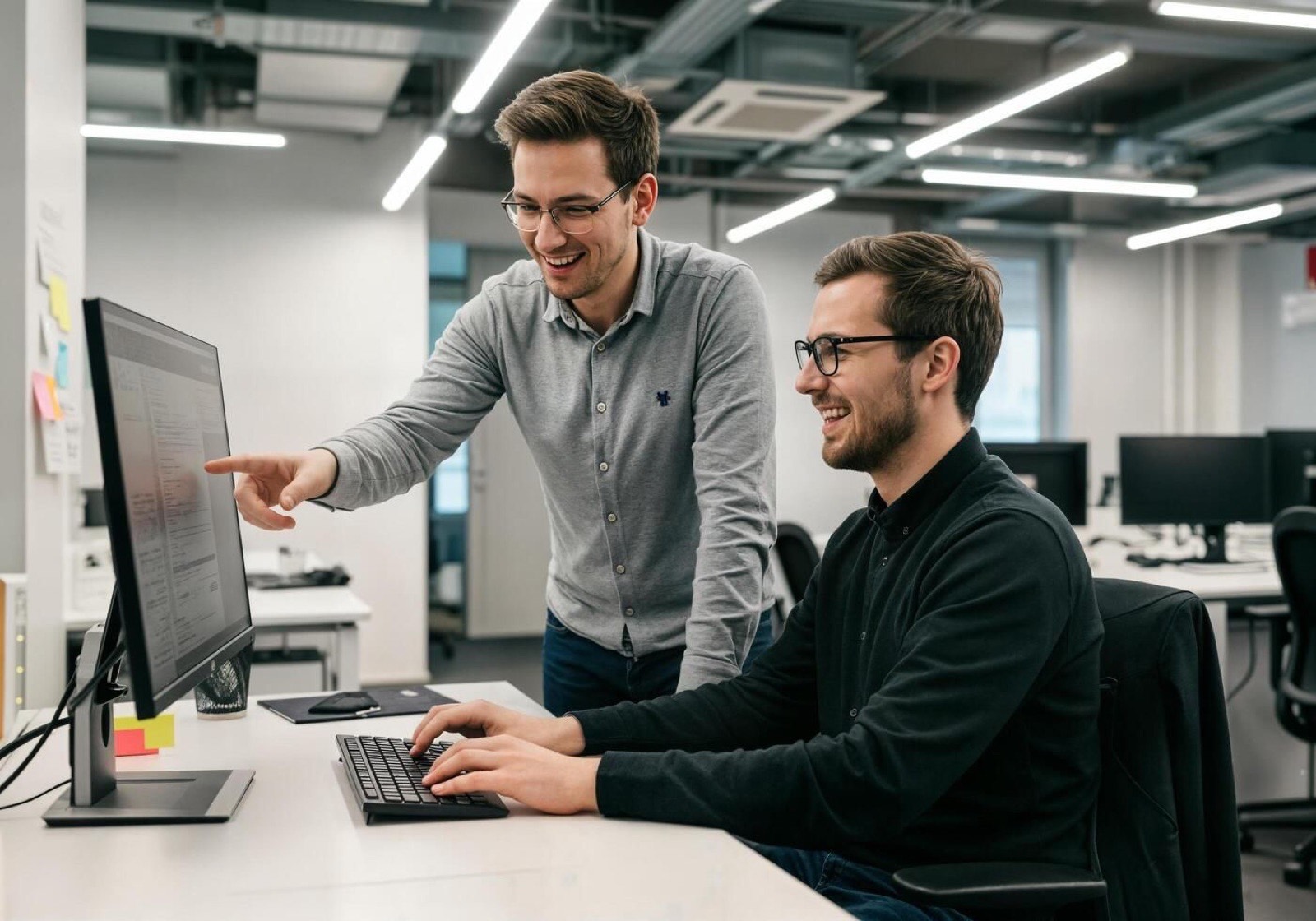 Two engineers reviewing code together at a desktop monitor
