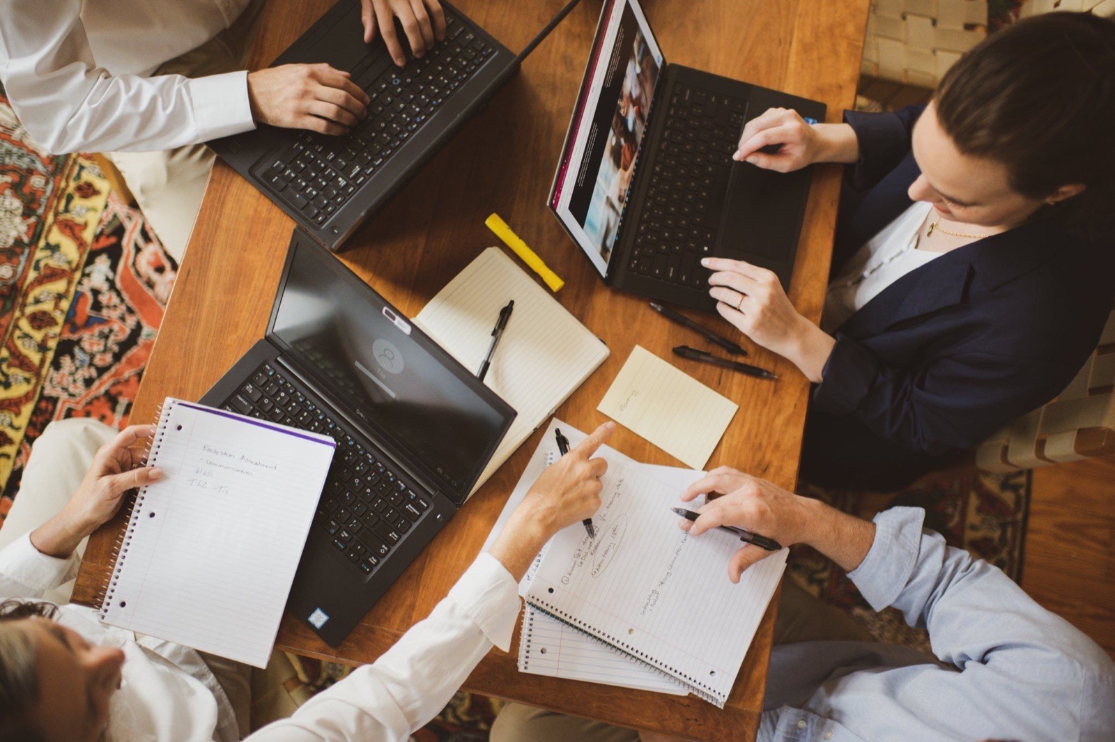 Overhead view of a small team taking notes around laptops on a wooden table