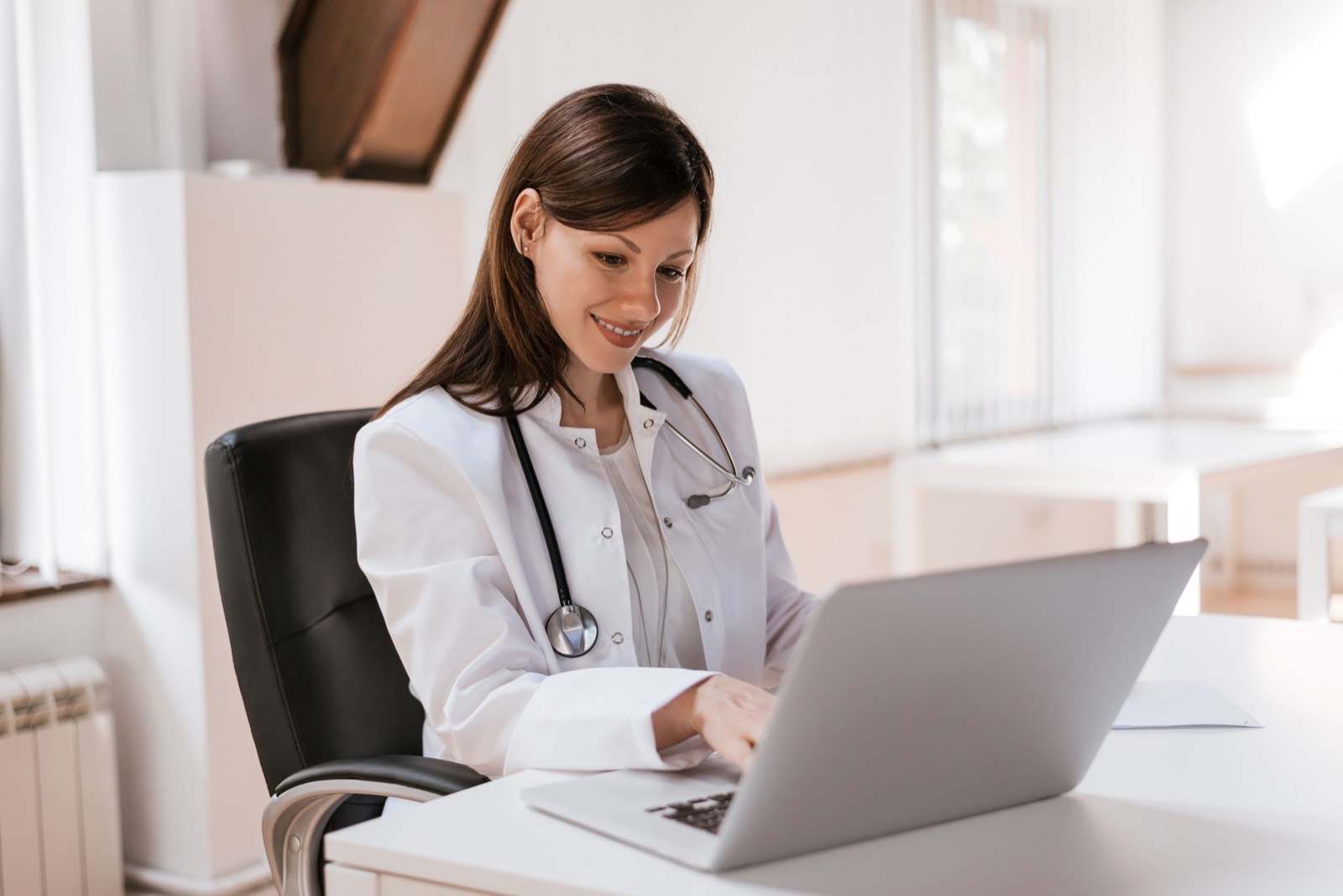 A doctor working on a laptop at a bright office desk