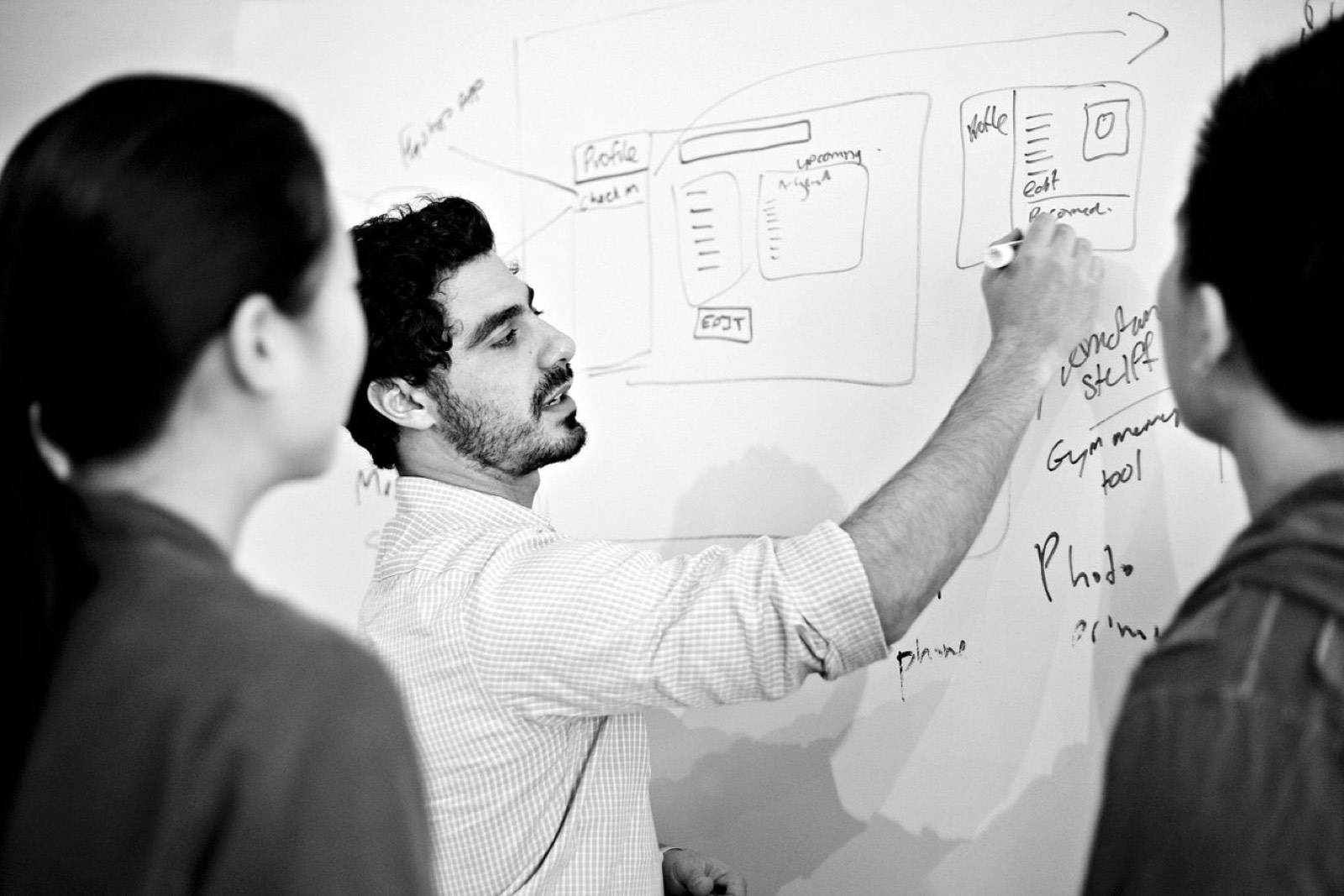 An engineer sketching a system on a whiteboard while two colleagues watch